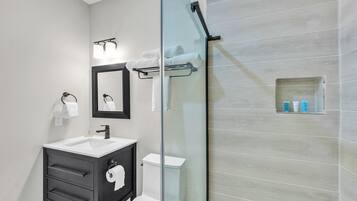 A modern bathroom with a glass-enclosed shower, a white sink, and a black vanity.