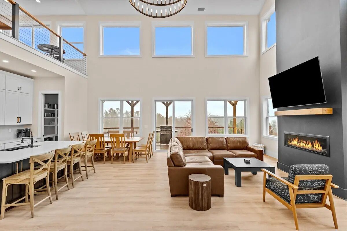 A spacious living area with a large sofa, a dining table, and chairs. There is a fireplace and a TV mounted on the wall.