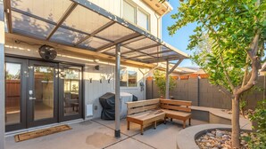 A covered patio with a bench, a small tree, and a stone planter.