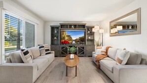 A modern living room with a large flat-screen TV, two sofas, a coffee table, and a large mirror.