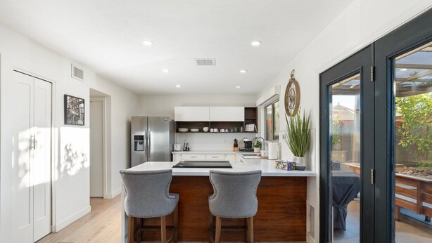 A modern kitchen with white cabinets, a central island, and two bar stools.
