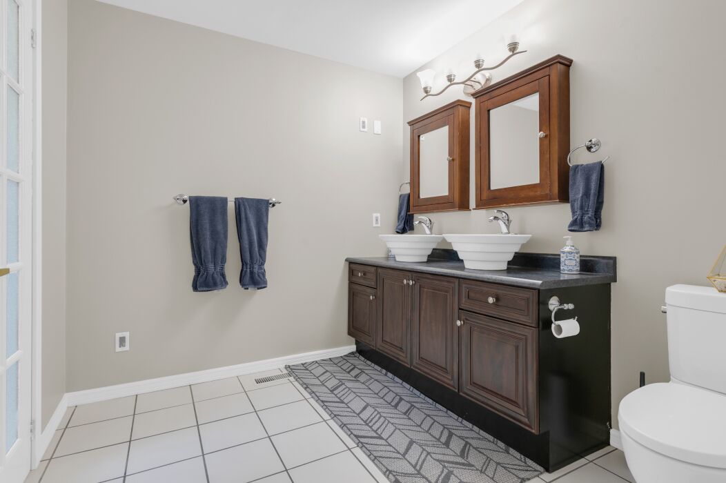 A bathroom with two sinks, a toilet, and a vanity with cabinets.