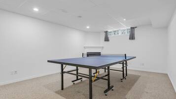 A room with a ping pong table, carpeted floor, white walls, and a fireplace.