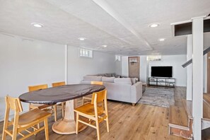 Un salon moderne comprenant une table à manger, des chaises, un canapé, un téléviseur à écran plat et un panier de basket.