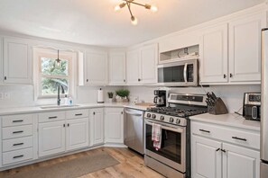 A kitchen with white cabinets, a stove, a microwave, and a coffee maker.