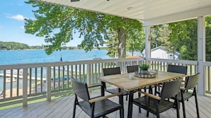 En overdækket terrasse med et bord og stole, med udsigt over en sø.