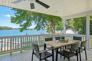 A covered outdoor deck with a table and chairs, overlooking a lake.