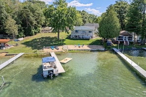 A house with a dock extending into a clear pond, surrounded by trees.