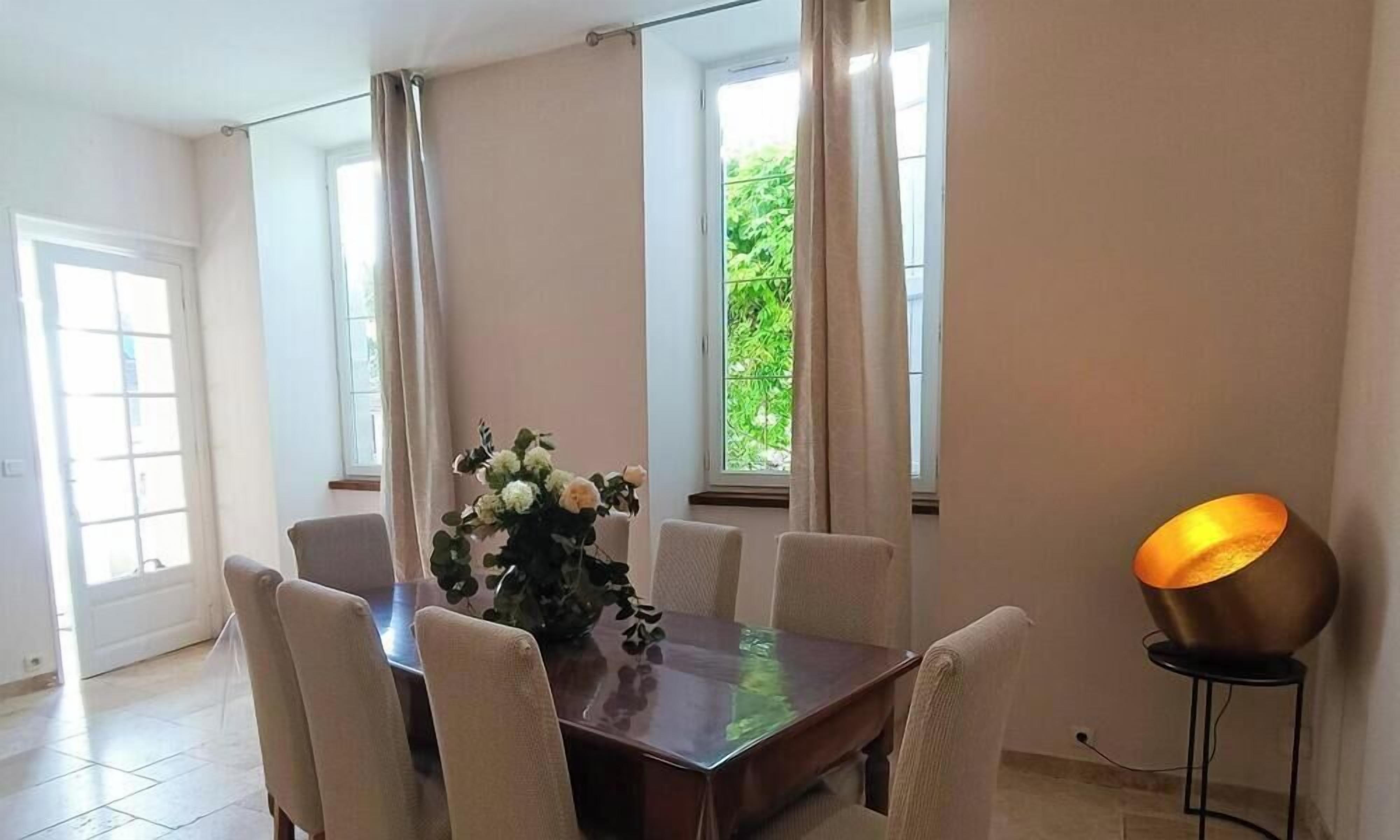 A dining area with a wooden table, six chairs, a vase of flowers, and a floor lamp.