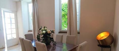 A dining area with a wooden table, six chairs, a vase of flowers, and a floor lamp.