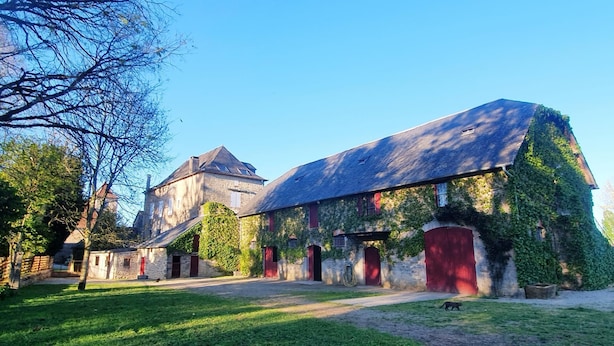 A historic building with stone walls and red doors, surrounded by a grassy area and trees.