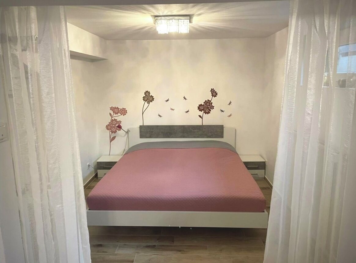 A bedroom with a bed, a nightstand, a wall-mounted light fixture, and a decorative wall piece.