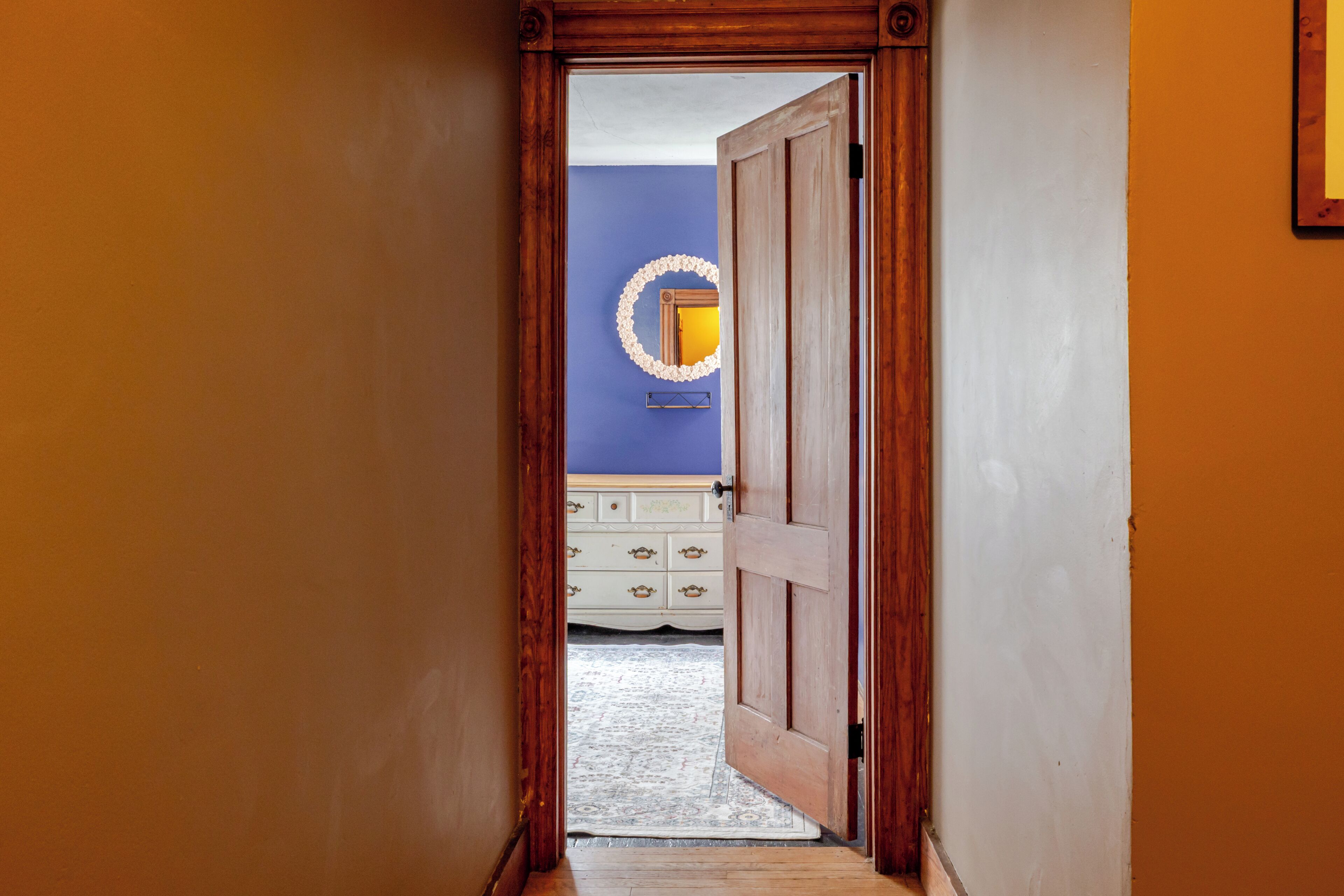 A hallway leading to a bedroom with a dresser and a mirror on the wall.