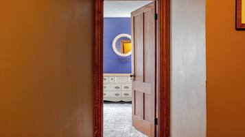 A hallway leading to a bedroom with a dresser and a mirror on the wall.