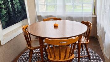 Una mesa de comedor redonda de madera con seis sillas, un centro de mesa con una calabaza pequeña y una alfombra estampada sobre un piso de madera.