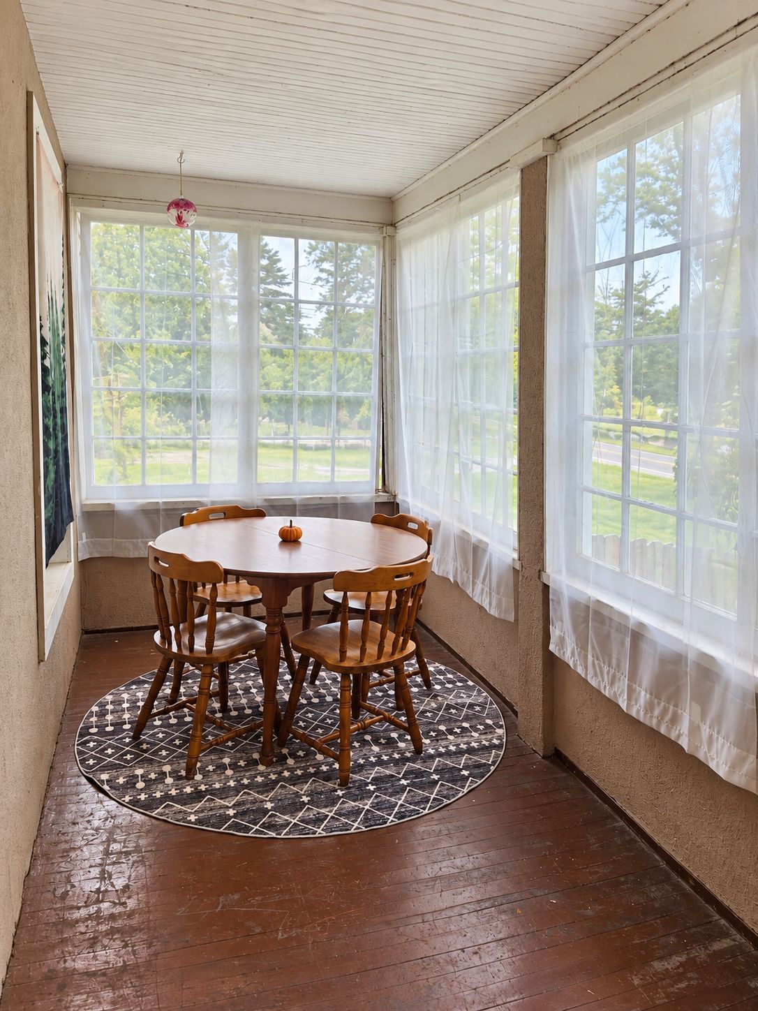 A sunroom with a wooden table and chairs, large windows, and a patterned rug.