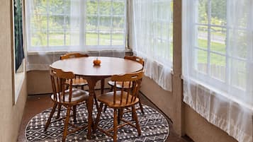A sunroom with a wooden table and chairs, large windows, and a patterned rug.