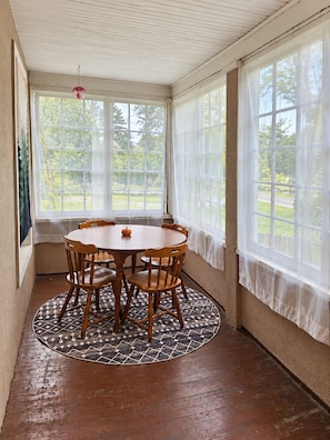 Un solarium con una mesa y sillas de madera, ventanas amplias y una alfombra estampada.