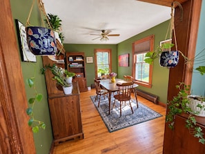 A dining area with a wooden table and chairs, a ceiling fan, and a view of the outdoors through windows.