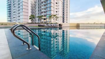 A swimming pool with a metal handrail, surrounded by a high-rise building with multiple balconies.