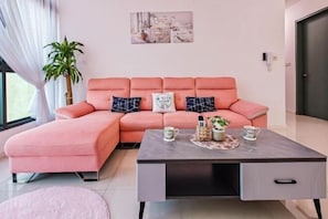 Uma sala de estar moderna com um sofá seccional rosa, uma mesa de centro cinza com objetos decorativos e uma obra de arte com tema urbano.