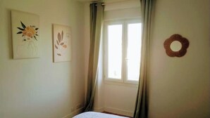 Une chambre à coucher avec un lit, une fenêtre avec des rideaux et deux œuvres d’art accrochées au mur.