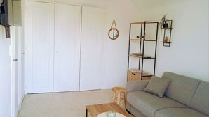 Un salon avec un canapé, une table basse sur laquelle est posée une bougie, une bibliothèque et une porte.