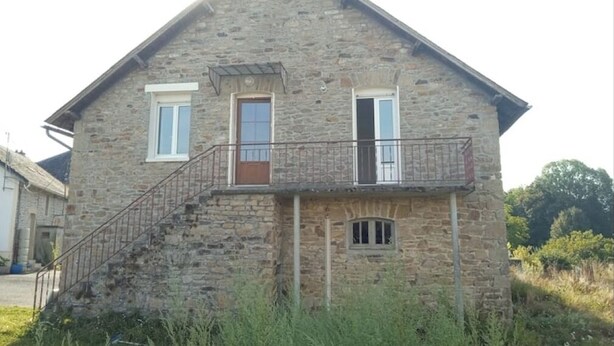 Une maison en pierre avec un balcon, un escalier et une petite fenêtre.