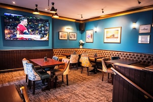 A restaurant with a large TV screen, cushioned booths, and framed pictures on the walls.