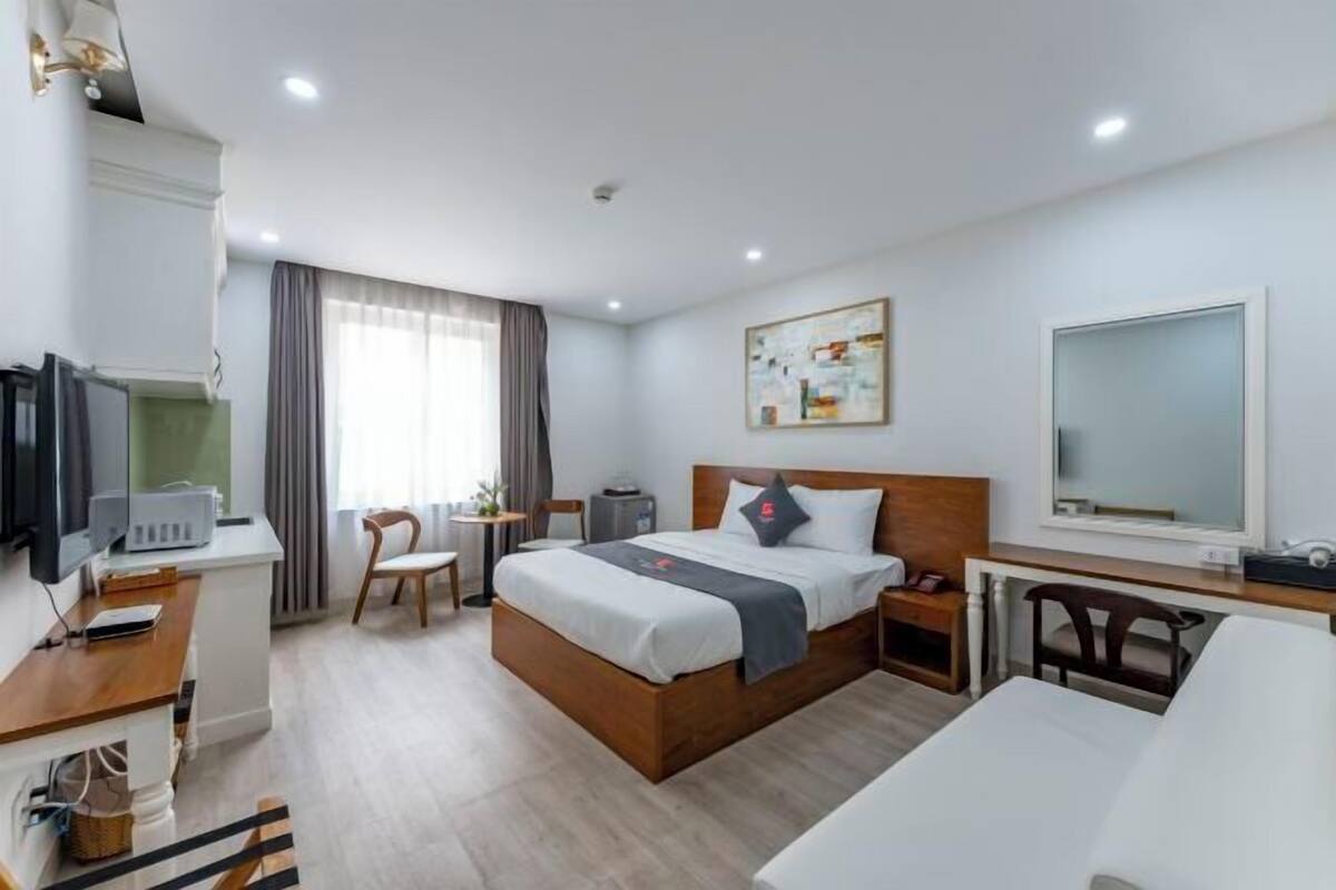 A hotel room with a bed, bedside table, desk, chair, and a television.