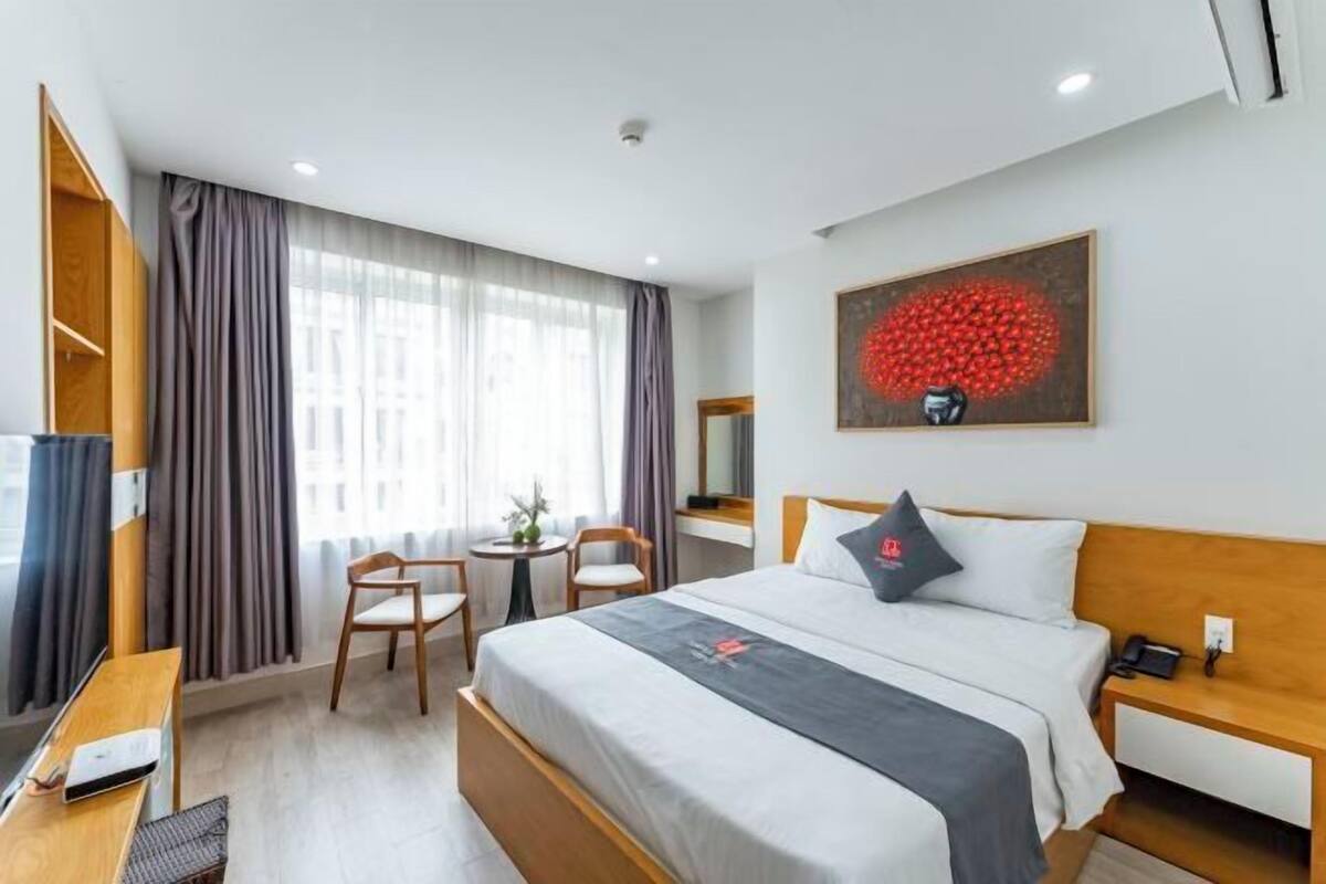 A hotel room with a bed, bedside table, chair, desk, and a painting on the wall.