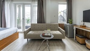 A modern hotel room with a sofa, a small table with items, a TV, a bed, and a view through the window. - Edoya Hotel Phu My Hung (Ho Chi Minh City)