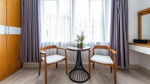 A room with a wooden wardrobe, a round table with two chairs, a vase with flowers, and a window with curtains. - Edoya Hotel Phu My Hung (Ho Chi Minh City)