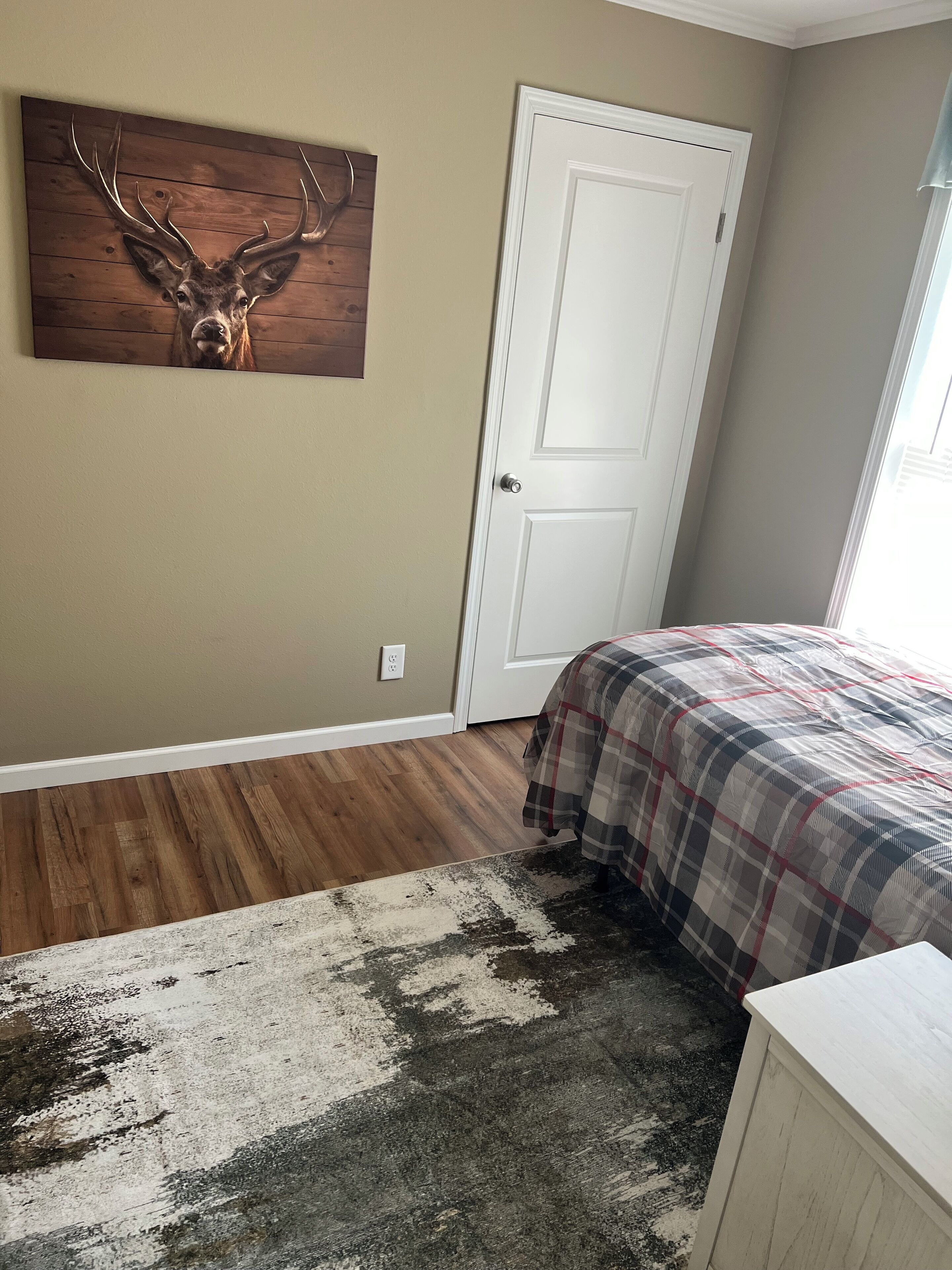 A bedroom with a plaid bedspread, a wooden deer head wall art, and a white door.