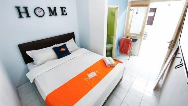 Una habitación de hotel con una cama, un cartel que dice 'HOME' en la pared y un baño visible a través de un arco.