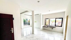 Una habitación amplia con piso de mármol, puerta de madera oscura y ventana con vista a follaje.