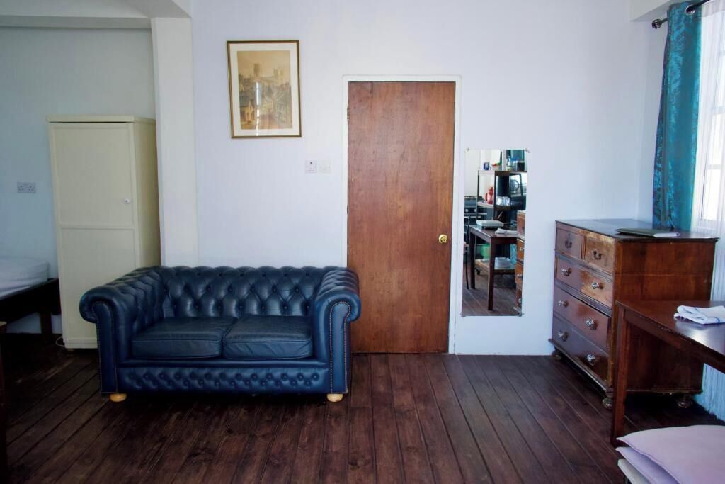 A room with a dark blue tufted sofa, wooden floor, a wooden door, a mirror, a dresser, and a cabinet.