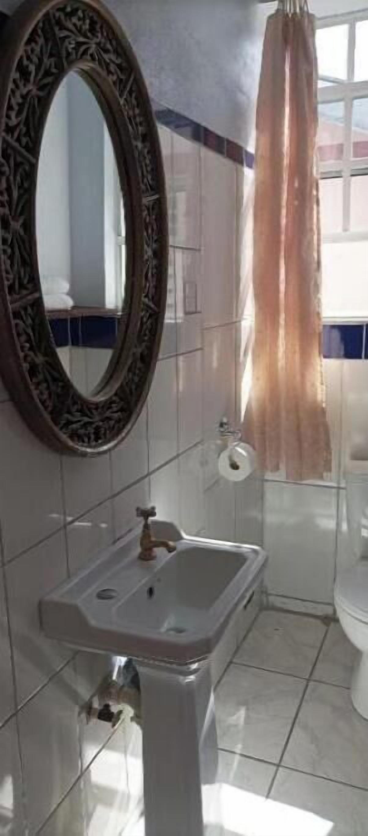 Un baño con lavamanos blanco, un espejo con marco decorativo, inodoro y cortina de ducha.