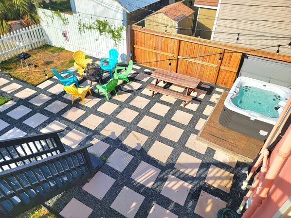 A backyard with a hot tub, a wooden deck, and colorful plastic chairs.