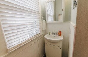 A bathroom with a sink, mirror, and window with blinds.