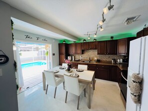 A modern kitchen with dark wooden cabinets, a tiled backsplash, and a dining area with white chairs and a table. - KM más que un hospedaje una experiencia que te abraza desde el primer momento. (Port Richey)