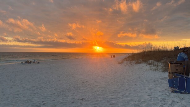 Een strand met een zonsondergang, zand en enkele mensen.