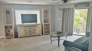 Een woonkamer met een televisie, houten planken, een glazen salontafel en een bank.