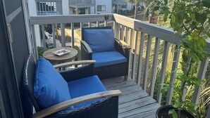 Een terras met rieten meubels en blauwe kussens, met uitzicht op een woongebied met huizen en een palmboom.