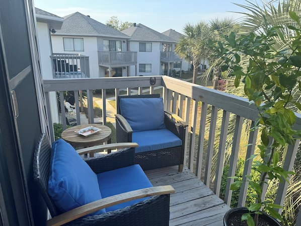 A deck with wicker furniture and blue cushions, overlooking a residential area with houses and a palm tree.