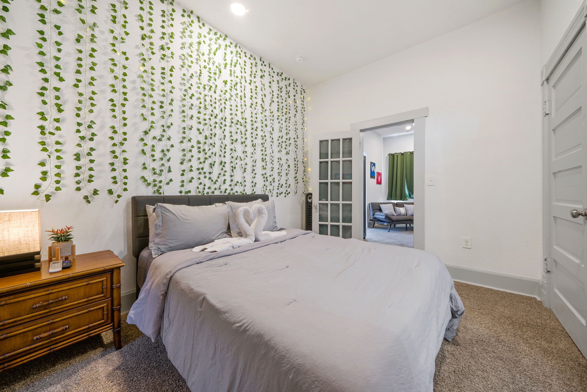 A bedroom with a bed, bedside table, and a wall with green leafy wallpaper.
