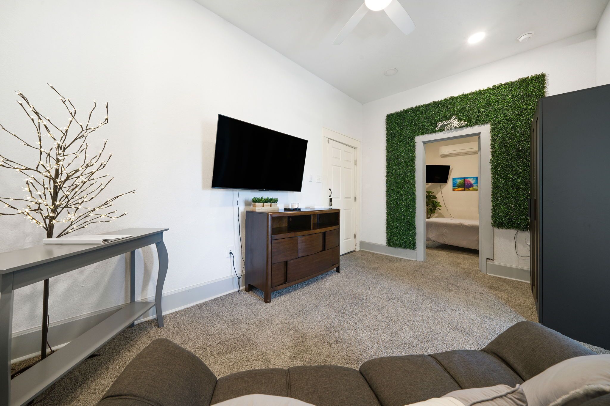 A modern living room with a flat-screen TV, a dark wooden entertainment unit, a grey console table, and a grey sofa.