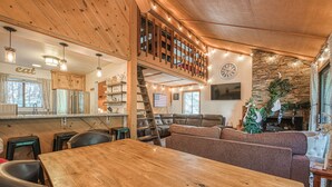 A cozy cabin interior with a wooden dining table, a loft bedroom with a staircase, and a living area with a fireplace. - Pet Friendly Condo w/ Hot Tub in Shaver Lake (Shaver Lake)