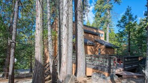 A lodge with a wooden deck, surrounded by tall trees, and a clear sky. - Pet Friendly Condo w/ Hot Tub in Shaver Lake (Shaver Lake)