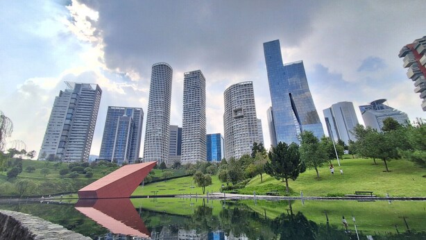 Un paysage urbain avec des gratte-ciel modernes et un parc doté d’un plan d’eau aux reflets changeants.